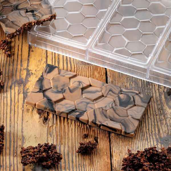 A Pavoni Polycarbonate chocolate bar mold on a counter with a chocolate bar in it.
