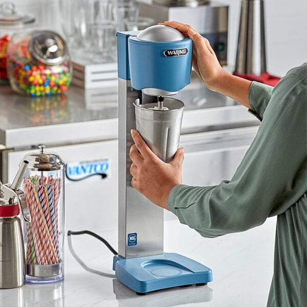 A woman using a Waring drink mixer to make a drink in a metal cup.