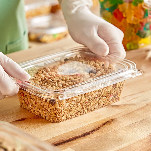 A gloved hand holding an Inline Plastics rectangular plastic container of granola.