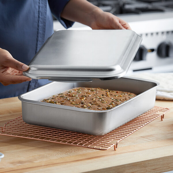 A woman holding a Nordic Ware rectangular aluminum cake pan with a cake inside.