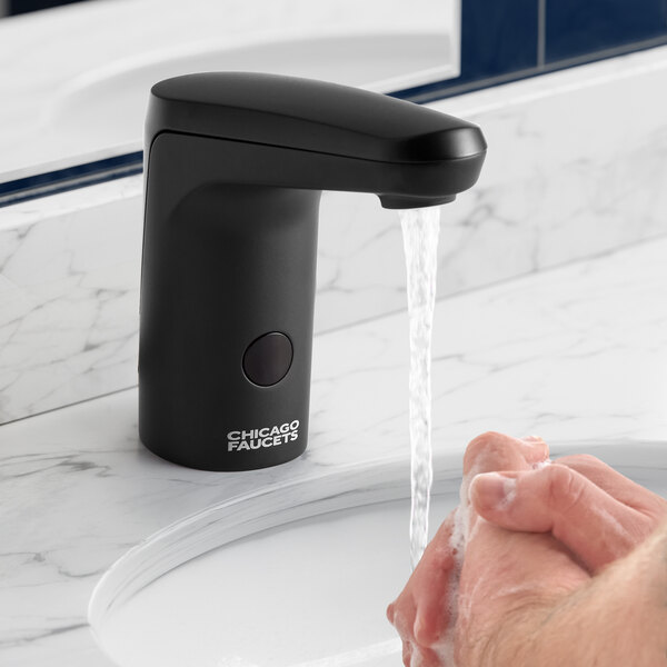 A person washing their hands under a black Chicago Faucets E-Tronic touchless faucet.