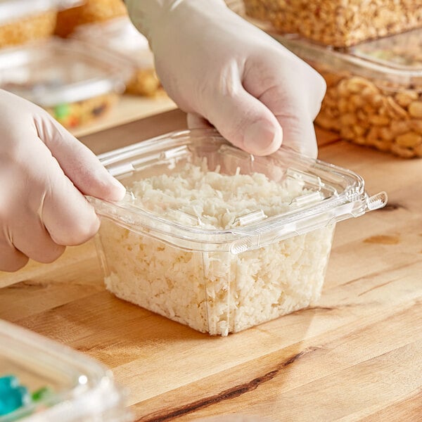 A person in gloves holding a Inline Plastics plastic container with rice in it.