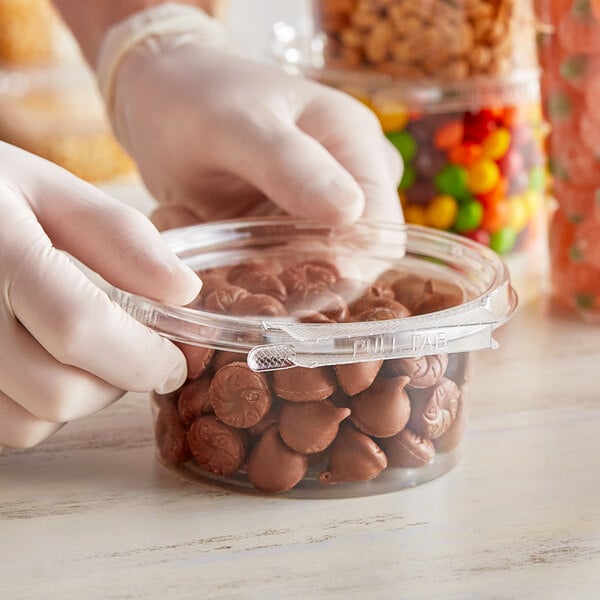 A person in gloves holding an Inline Plastics Safe-T-Fresh plastic container of chocolate candies.