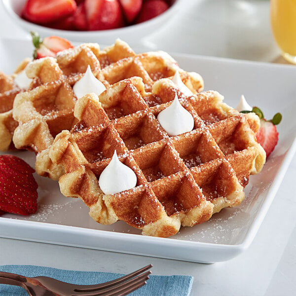 A white plate with White Toque Liege waffles topped with whipped cream and strawberries.