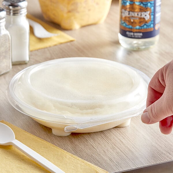 A hand holding a white Inline Plastics Safe-T-Chef plastic container with food and a white plastic spoon on a yellow napkin.