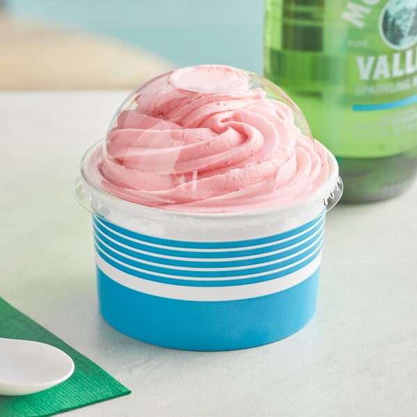 A blue Choice paper frozen yogurt cup with a dome lid filled with pink frozen yogurt on a counter.