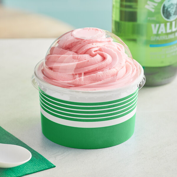 A green paper frozen yogurt cup with a dome lid filled with pink frozen yogurt on a counter.