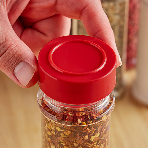 A person holding a red 48/485 unlined polypropylene cap over a jar of spices.
