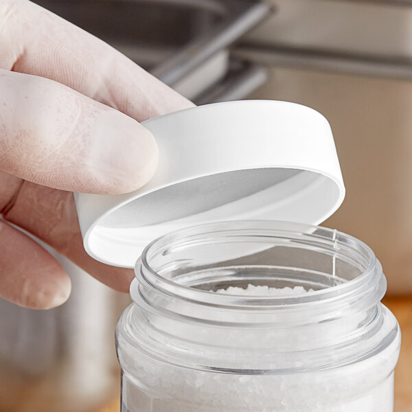A hand holding a 63/485 white polypropylene spice cap opening a white container.