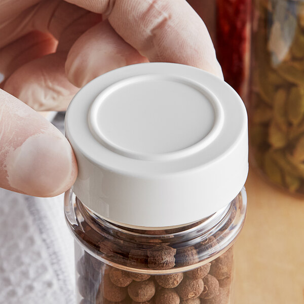 A person holding a white container with a 48/485 white unlined polypropylene spice cap on it.