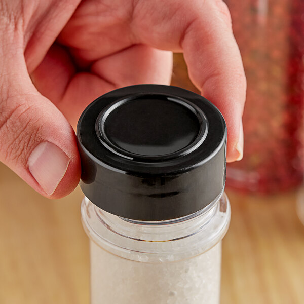 A person holding a small container of salt with a black polypropylene spice cap.
