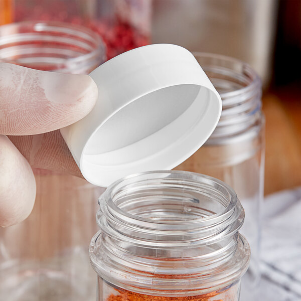 A person holding a white 48/485 polypropylene spice cap over a small glass container.