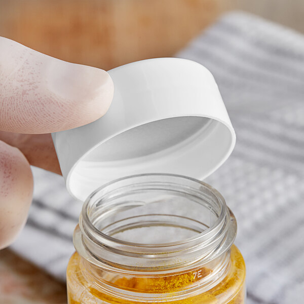 A person's finger opening a white polypropylene spice cap on a jar of yellow powder.
