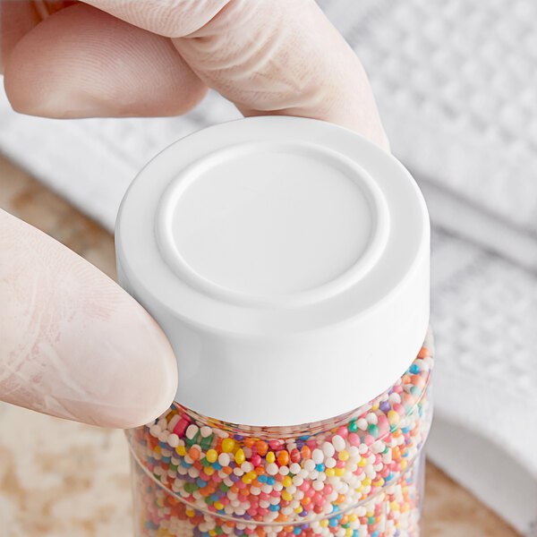 A person holding a jar of colorful sprinkles with a white polypropylene spice cap.