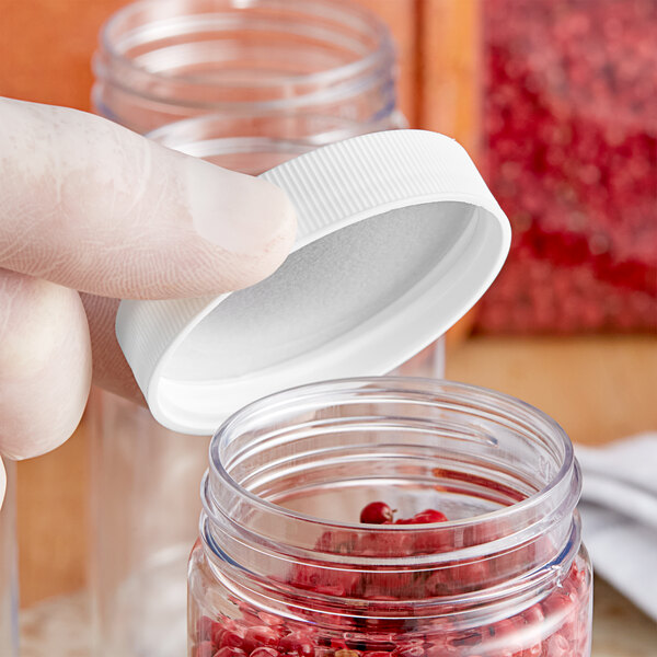 A person using a finger to open a 53/400 white polypropylene cap over a jar of red berries.