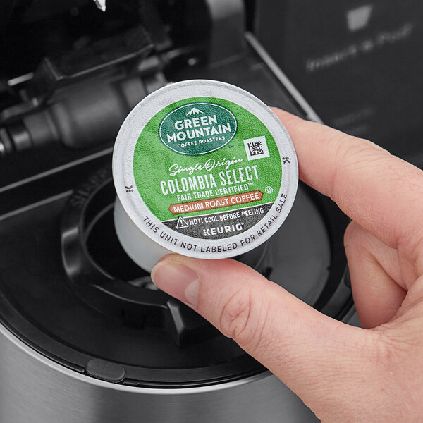 A hand holding a Green Mountain Coffee Roasters Colombian Select K-Cup Pod over a coffee machine.