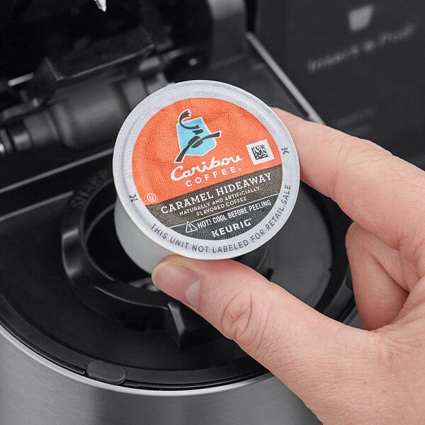 A hand holding a Caribou Coffee Caramel Hideaway K-Cup Pod container.