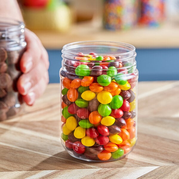 A hand holding a clear plastic jar of candy.