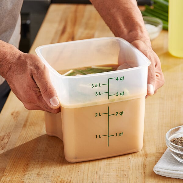 A person holding a Cambro FreshPro square polypropylene container of soup.