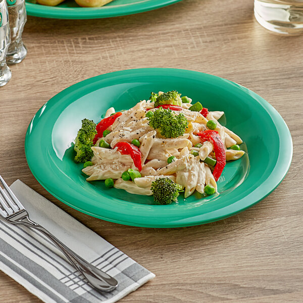 A green Acopa Foundations wide rim melamine plate with pasta, broccoli, and vegetables with a fork on the table.