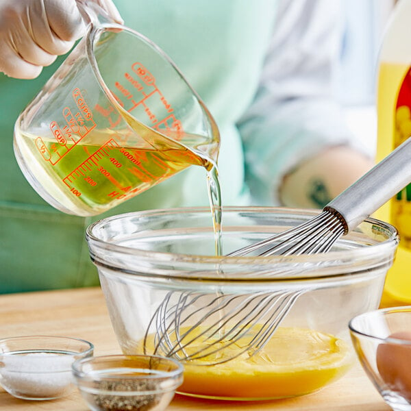 A person pouring Mazola Canola Oil into a bowl with a whisk.