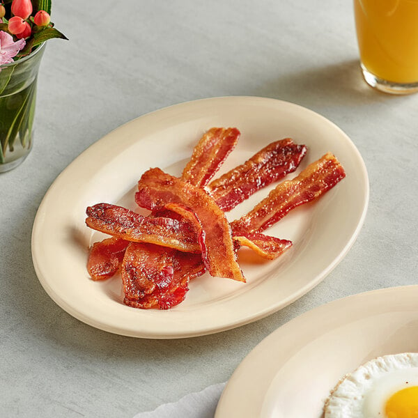 An Acopa tan melamine platter holding bacon and eggs on a table.