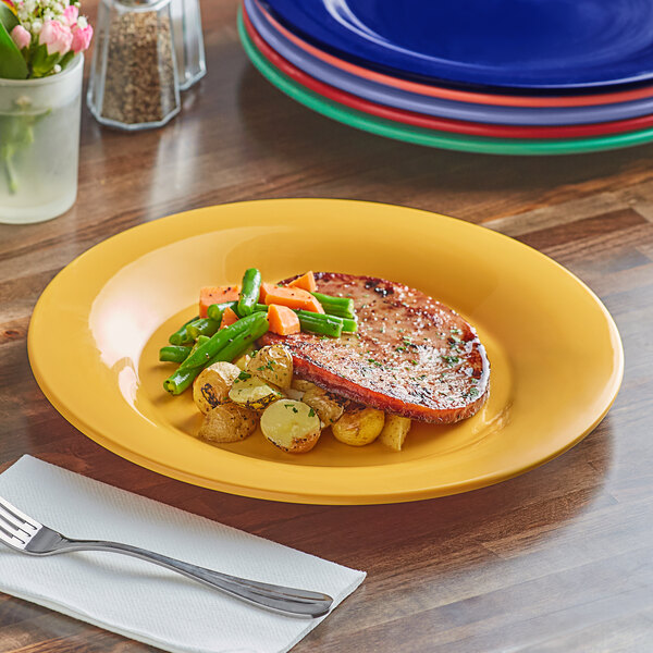 An Acopa Foundations yellow wide rim melamine plate with food on it and a silver spoon on a white napkin.