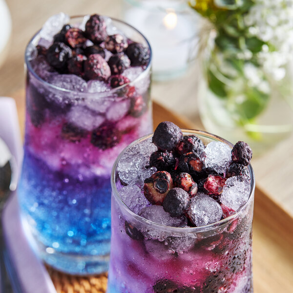 A glass of blue and purple drink with Mixologist's Garden freeze-dried blueberries on the table.