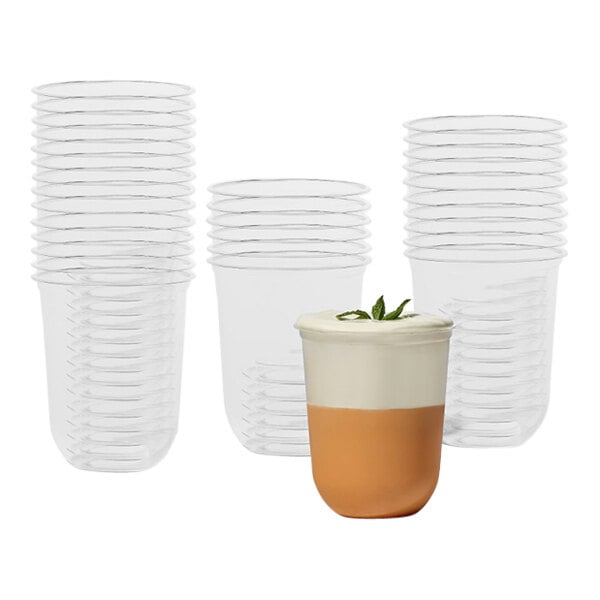 A Tossware Natural rounded bottom plastic cup with a brown liquid next to a stack of clear plastic cups.