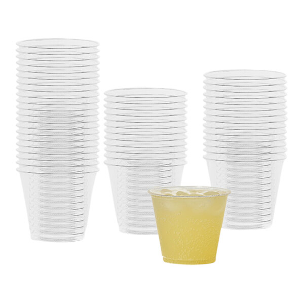 A stack of Tossware clear plastic cups with a yellow liquid in them.