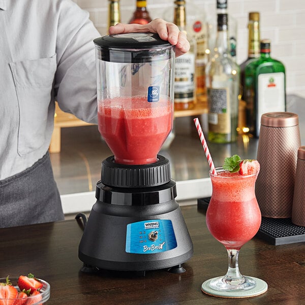 A person using a Waring BevBasix commercial bar blender to make a red drink.
