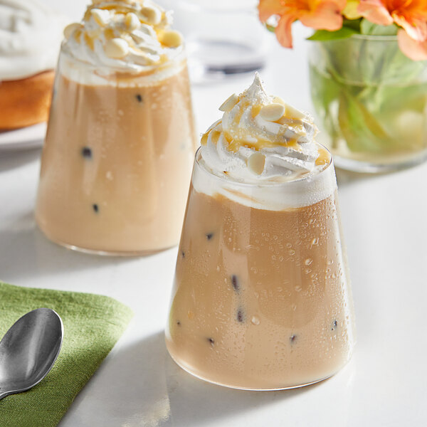 Two glasses of coffee with Guittard Sweet Ground White Satin Chocolate Flavoring Sauce and whipped cream.