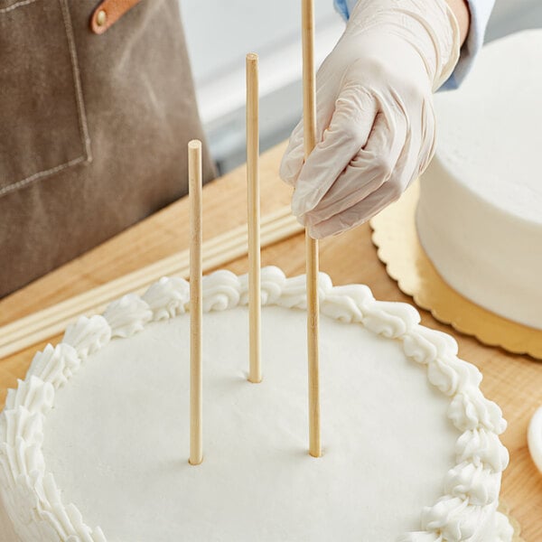 A person inserting Wilton bamboo dowel rods into a cake.