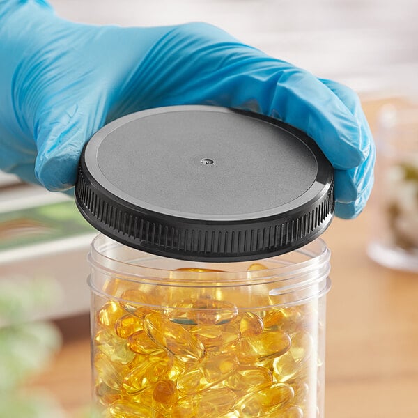 A hand in a blue glove holding a 89/400 black plastic cap over a jar of yellow pills.