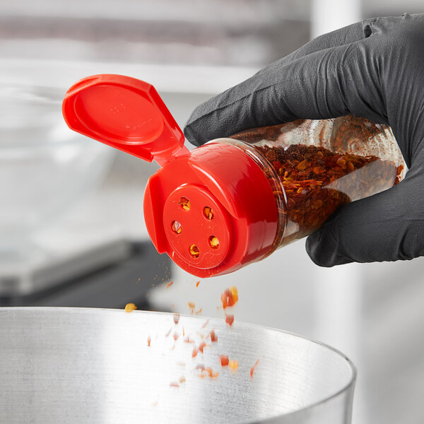 A hand in a black glove using a 43/485 Red Flip and Sift Lid to pour chili powder into a bowl.