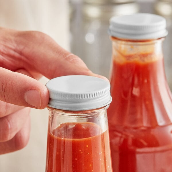 A hand holding a jar of red sauce with a white metal lid.