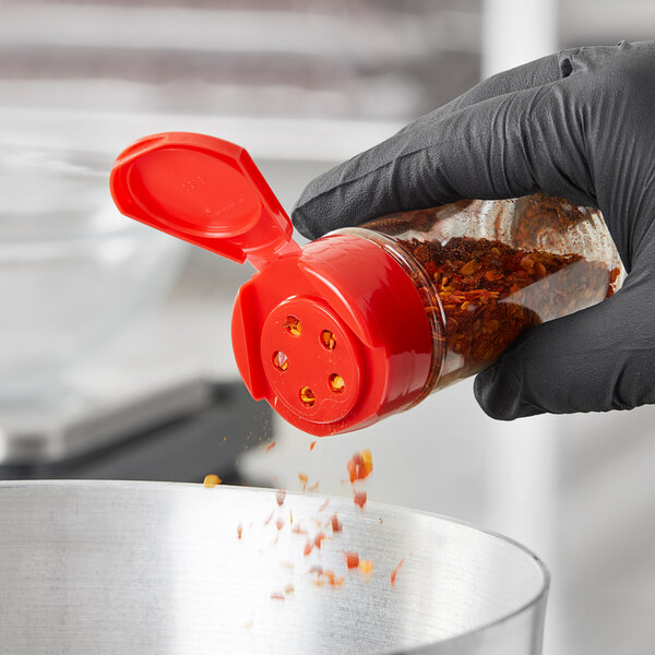 A hand in a black glove using a 43/485 red flip and sift spice lid to pour seasoning into a container.