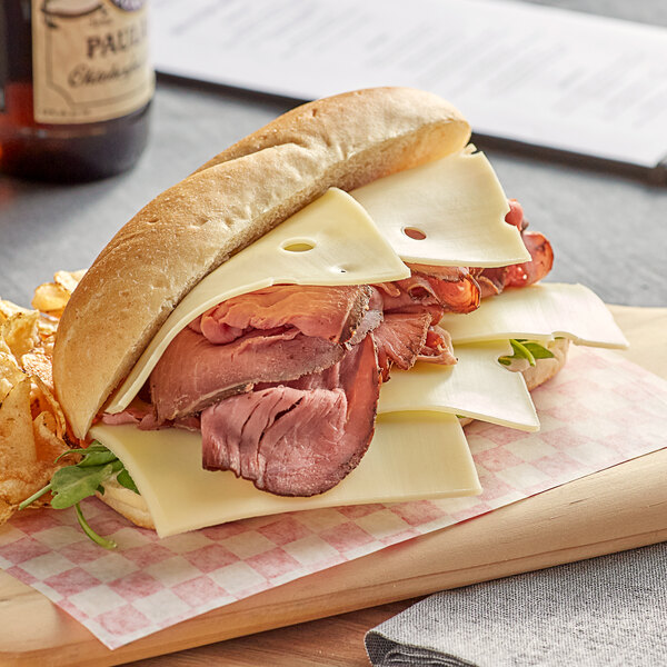 A sandwich with Tillamook Swiss cheese, meat, and cheese on a cutting board.