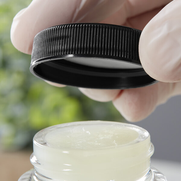 A hand in gloves using a black ribbed plastic cap to seal a jar.