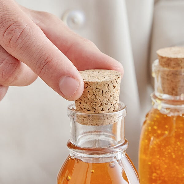 A person's hand using a cork to seal a bottle of honey.