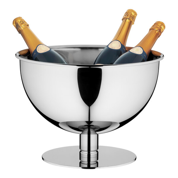 A WMF stainless steel punch bowl on a table with a champagne bottle and two glasses inside.
