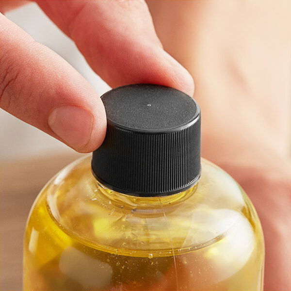 A hand holding a bottle of liquid with a 24/410 black plastic cap.