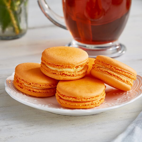 A white plate of Coco Bakery mango passionfruit macarons with orange shells.