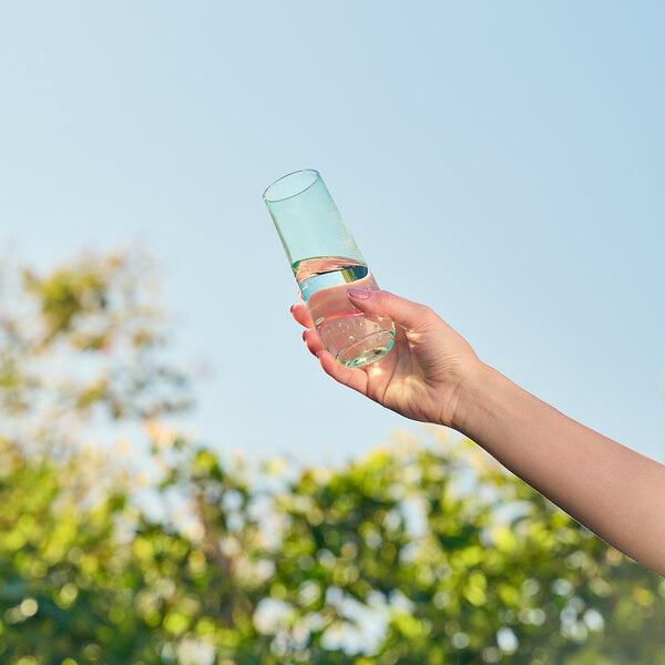 A hand holding a mint green Tossware flute glass filled with water.