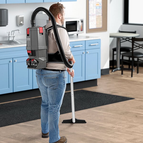 A man wearing a backpack vacuuming in a professional kitchen.