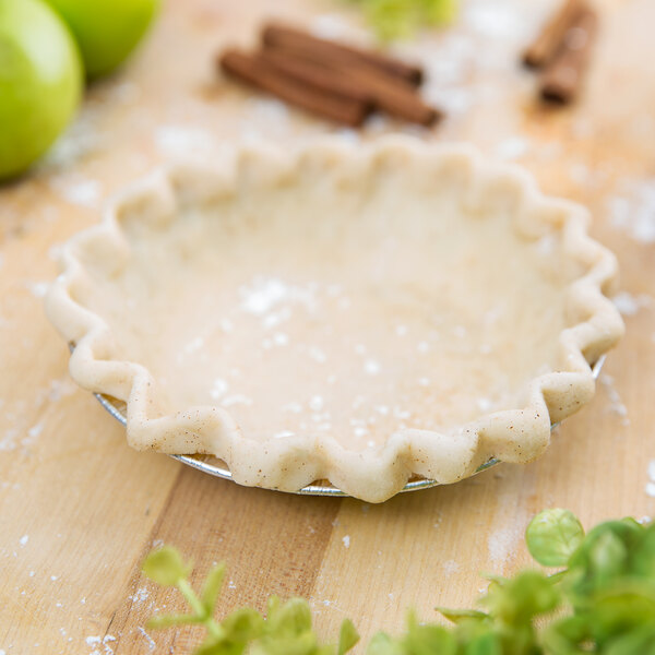 A Baker's Lane medium depth foil pie pan with a pie crust in it on a table with a green apple.