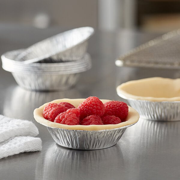 A Baker's Lane foil tart pan with raspberries in it on a counter.