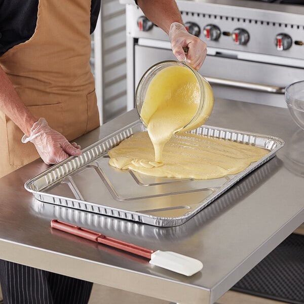A person pouring yellow liquid into a Baker's Lane foil cake pan.