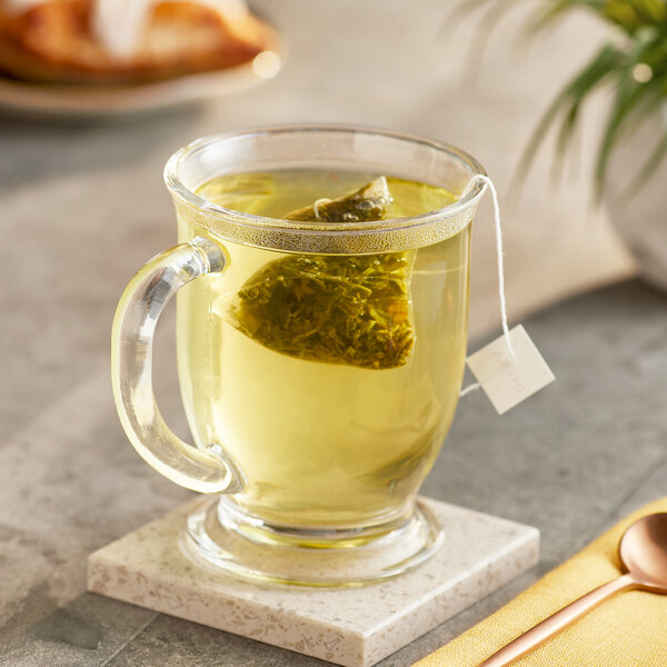 A glass mug of green tea with a Dona Supertwist Green Tea sachet in it.