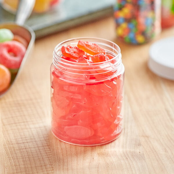 A clear plastic jar filled with orange jelly, candy, and fruit slices on a table.